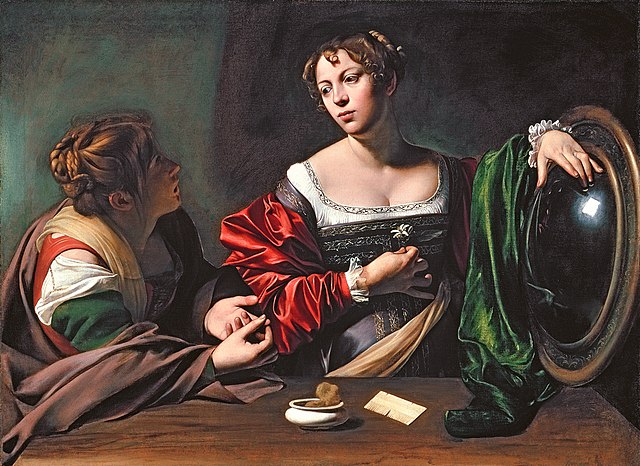 Caravaggio's painting 'Martha and Mary' from 1598.  To the left sits Martha, wrapped in a plain cloak, leaning across a table. Her face is in shadow as she offers advice to Mary. To the right stands Mary Magdalene, in red satin jacket, her face lit as she considers. Mary twirls a flower in one hand, her other rests upon a large round mirror, which reflects one bright window.