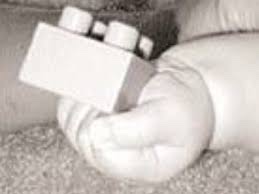 B/w photo of a newborn baby’s hand gripping a Lego brick